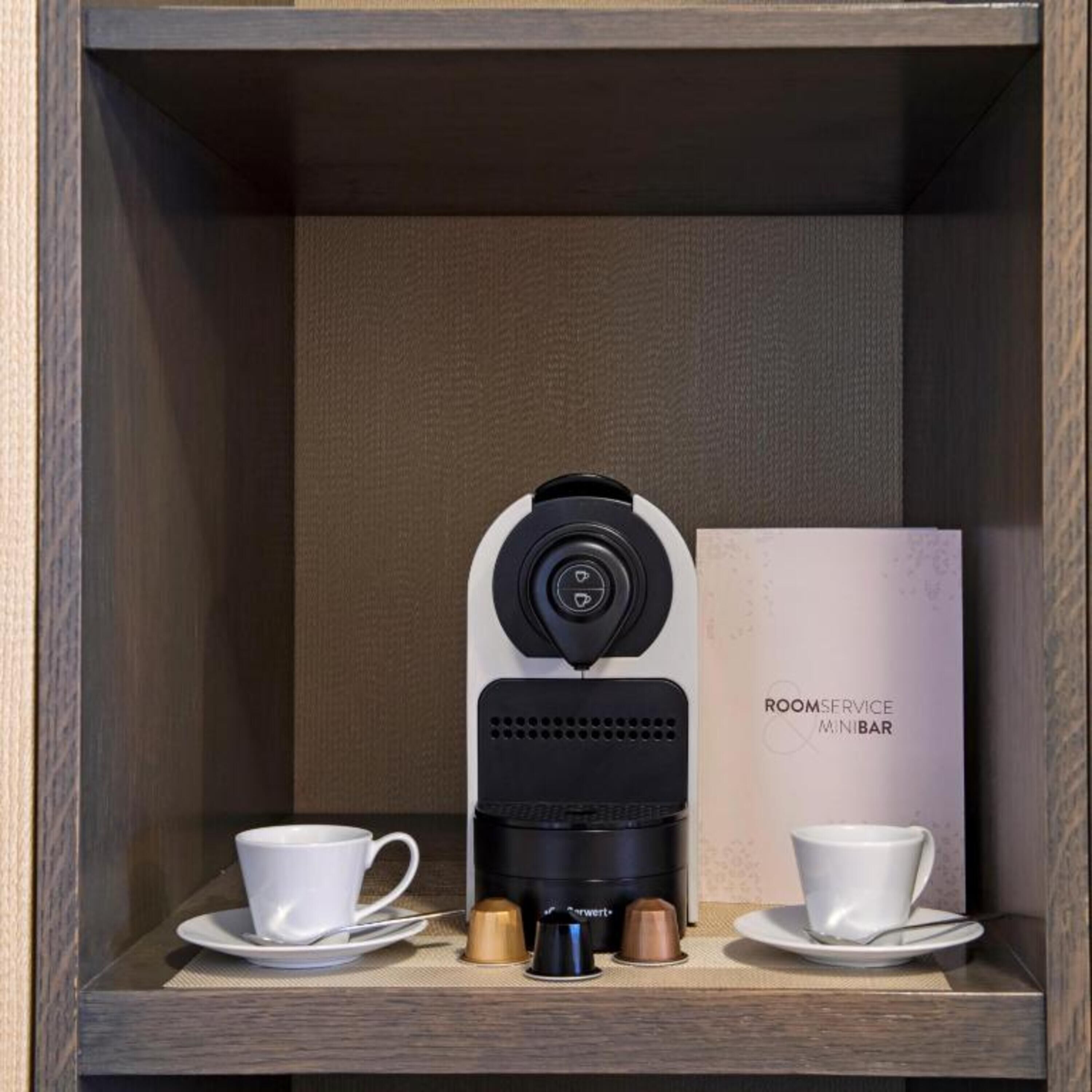 A coffee machine with two cups and a box labeled "ROOMSERVICE MINIBAR".