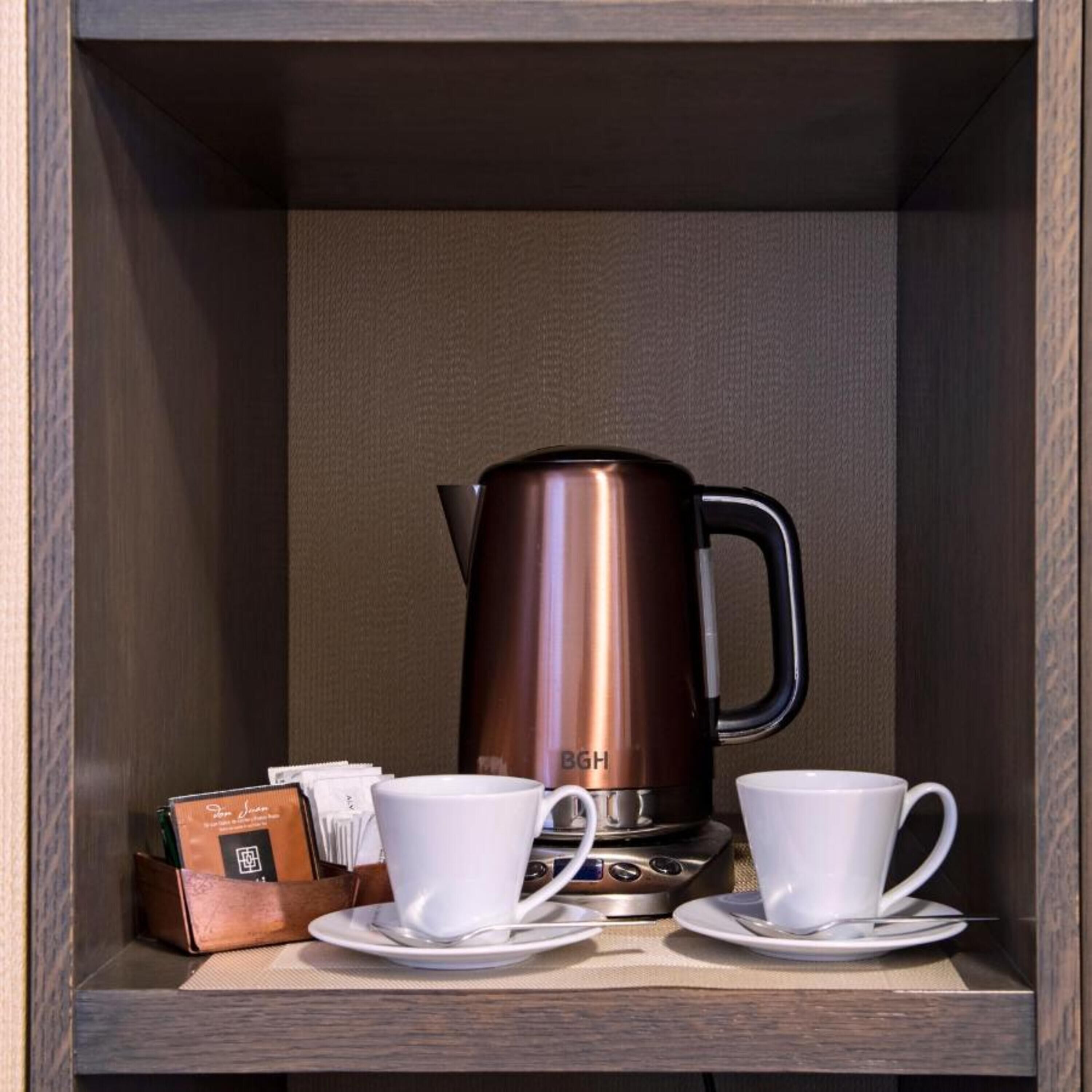 A coffee station with a coffee maker, two cups, and a sugar container.