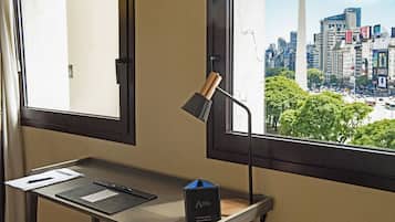 A desk with a lamp, papers, and a box, overlooking a cityscape with a tall monument.