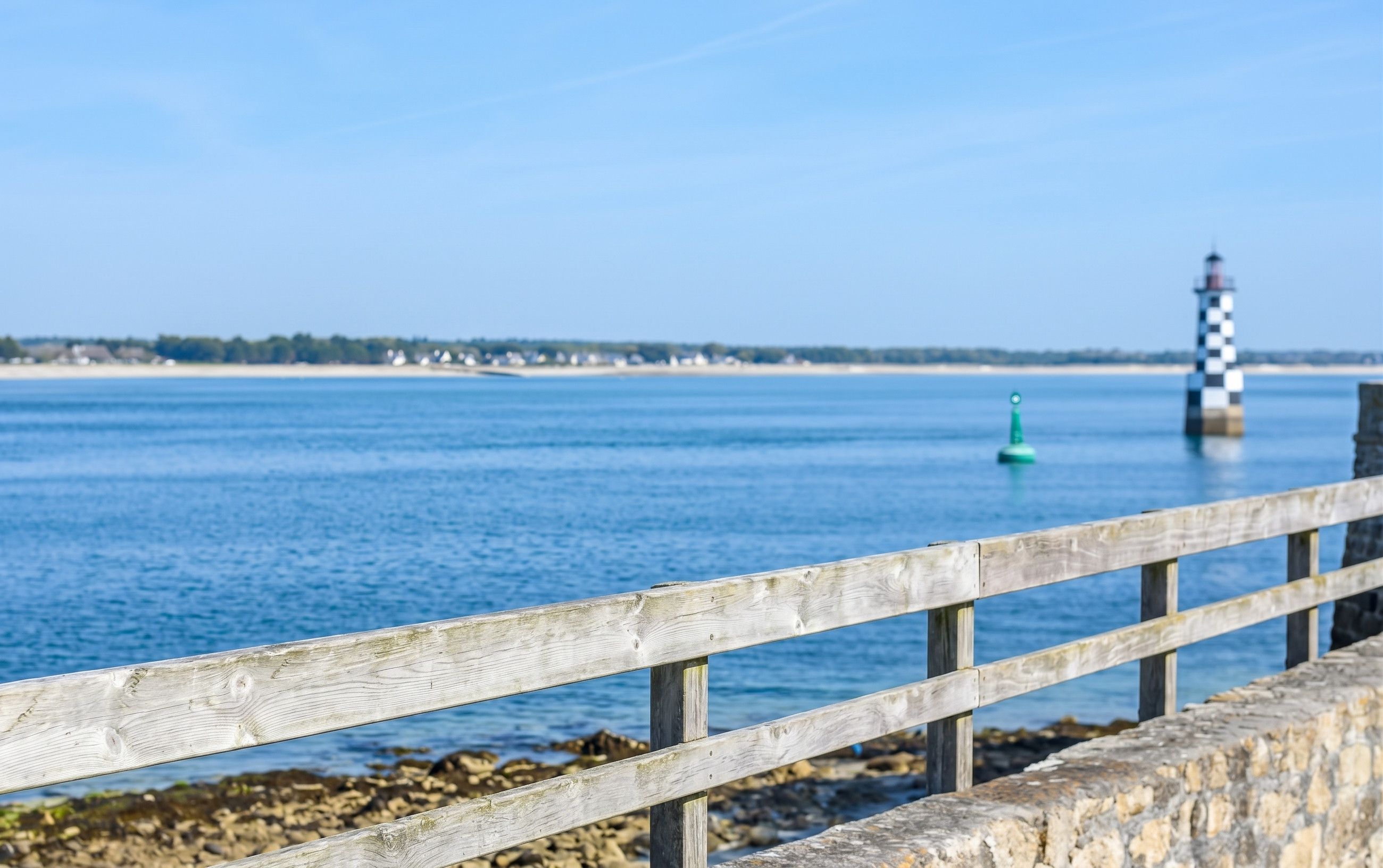 A wooden pier with a stone balustrade leading to a rocky shoreline.