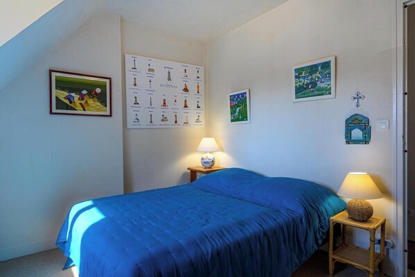 A bedroom with a blue bedspread, two bedside lamps, a framed picture, a map, and a small decorative item on the wall.