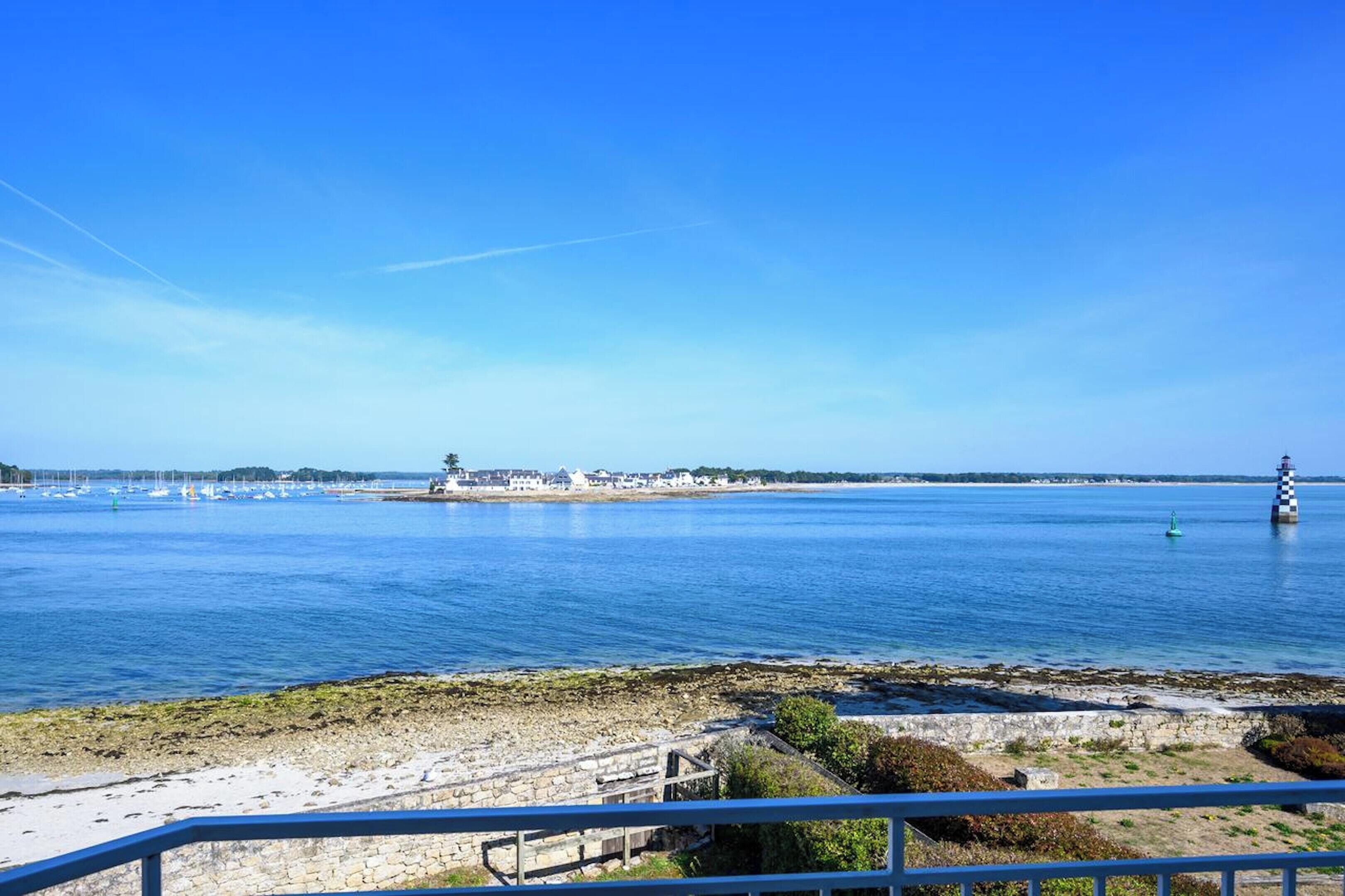 Blick auf die Küste mit einem Leuchtturm, ruhiger See und einem Steinsteg.
