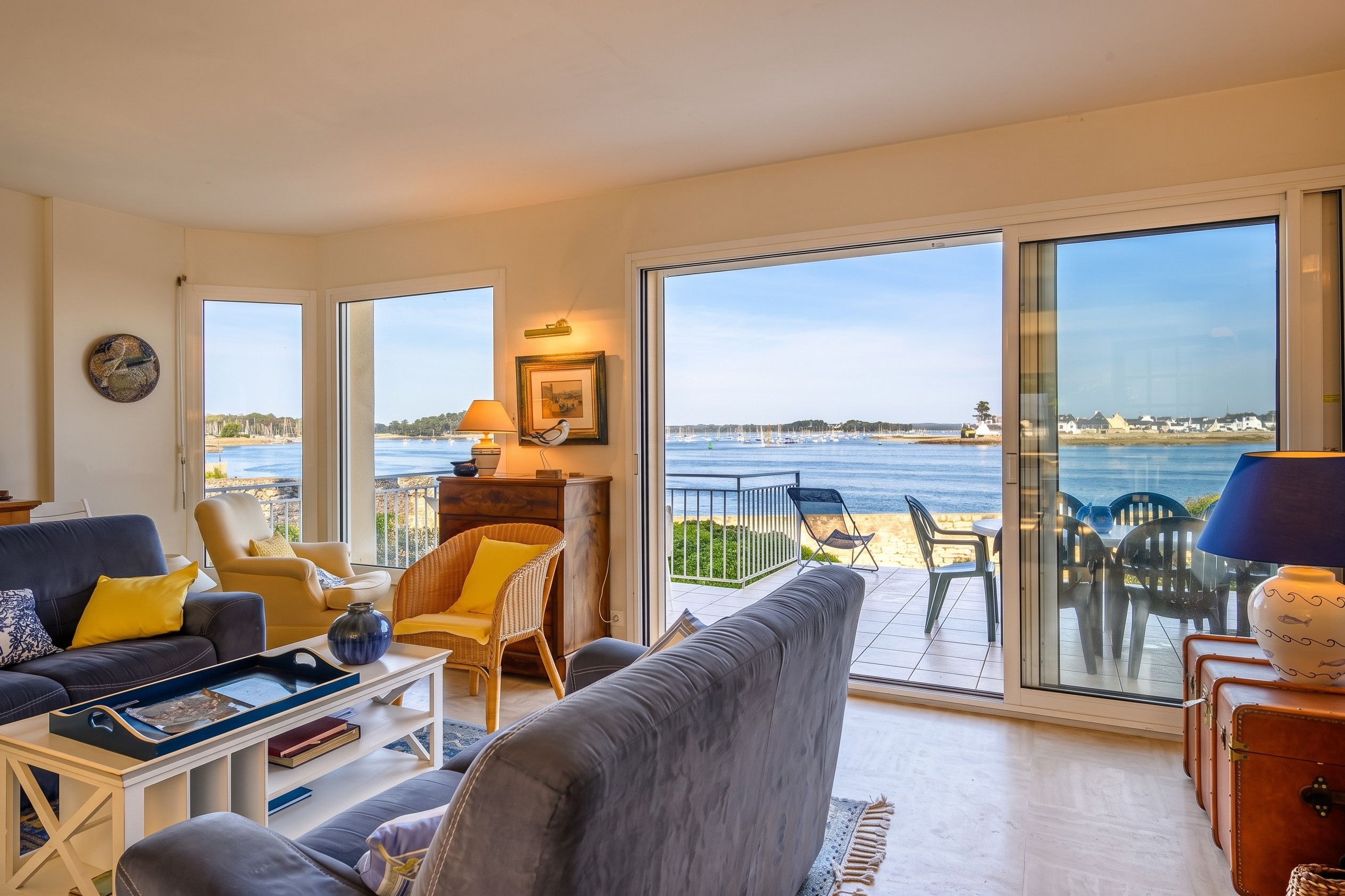 A living room with a view of the sea, furnished with a sofa, chairs, and a table.