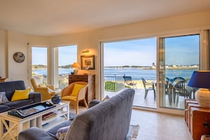 A living room with a view of the sea, furnished with a sofa, chairs, and a table.