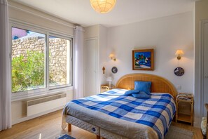 Een slaapkamer met een bed, een raam, een wandklok en een schilderij.