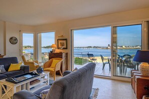 A spacious living room with a large sliding glass door leading to a balcony with a view of the sea.