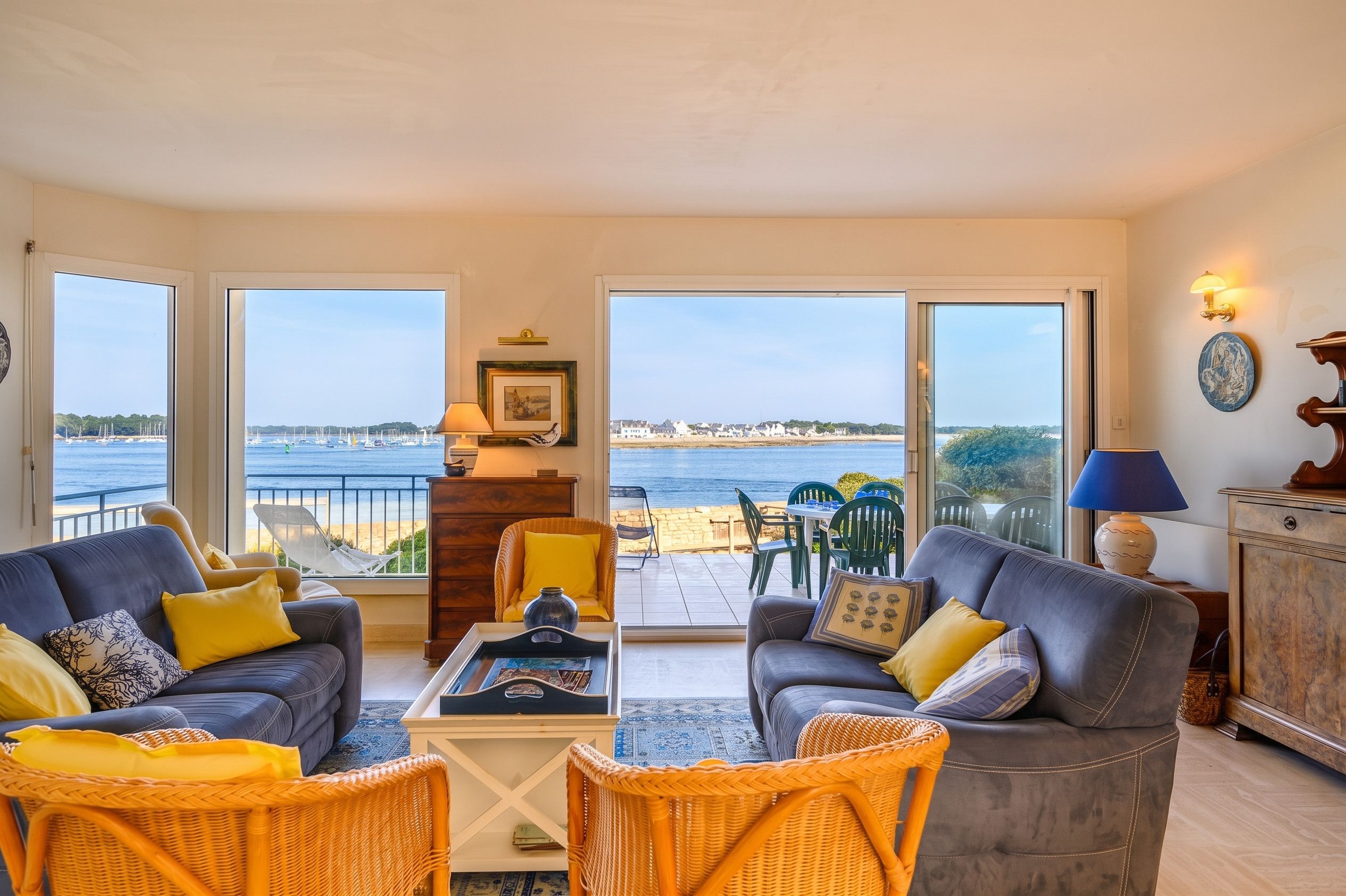 Un vaste salon avec vue sur la mer, aménagé avec deux canapés, une table basse et des fauteuils en osier.