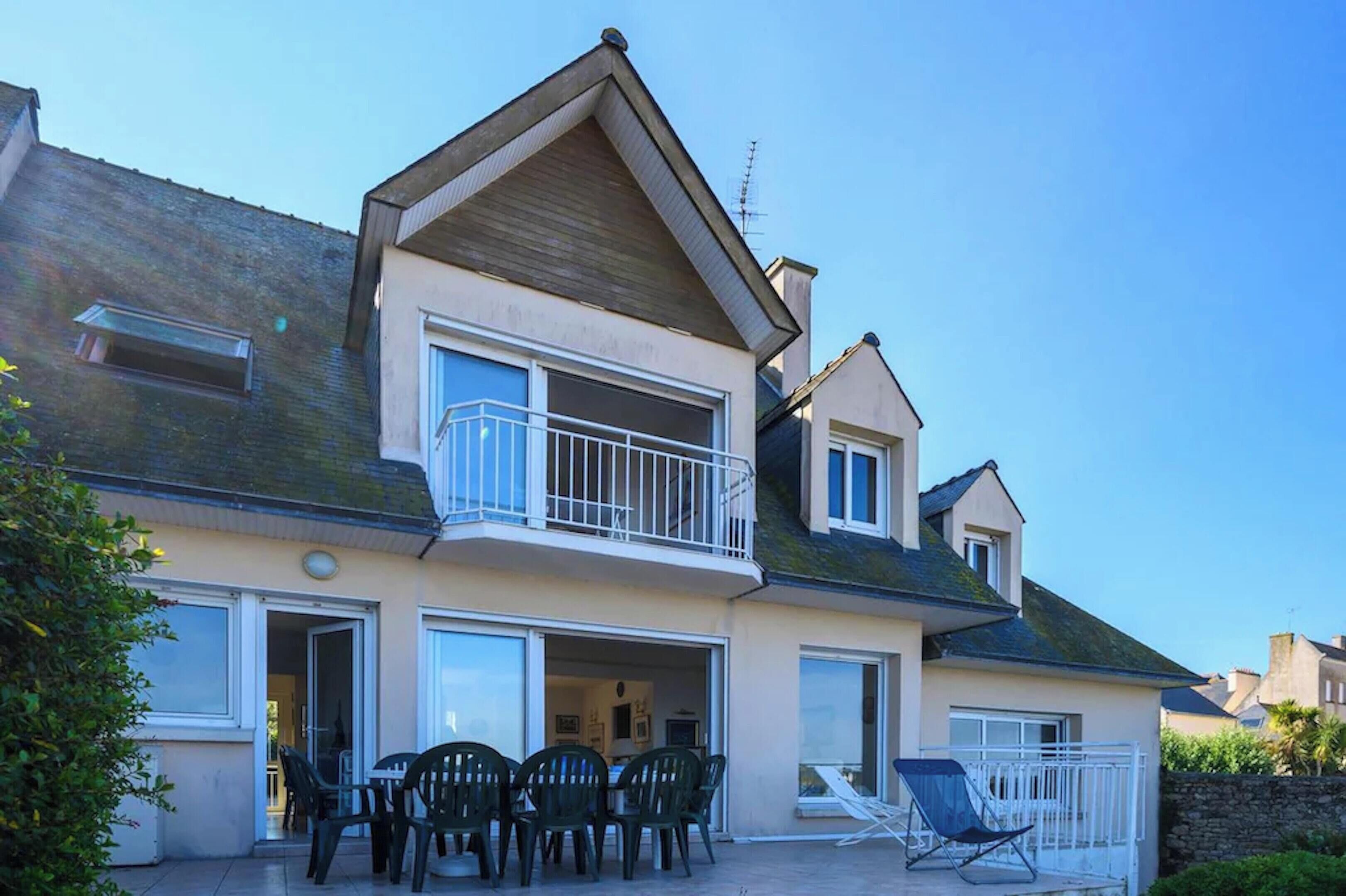 Une maison à deux étages dotée d’un balcon, d’une terrasse avec des chaises et d’une porte coulissante.