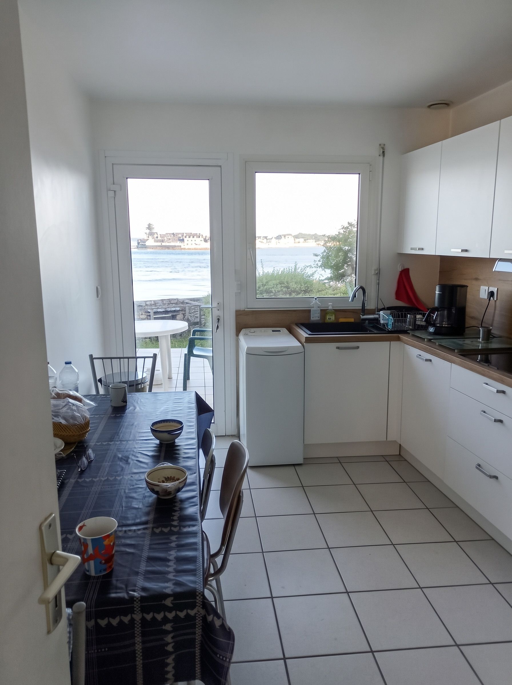 Une cuisine compacte avec vue sur la mer, une table à manger avec des chaises et un petit réfrigérateur.