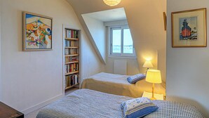 Une chambre avec deux lits, une bibliothèque, une fenêtre donnant sur un beau paysage et une lampe.