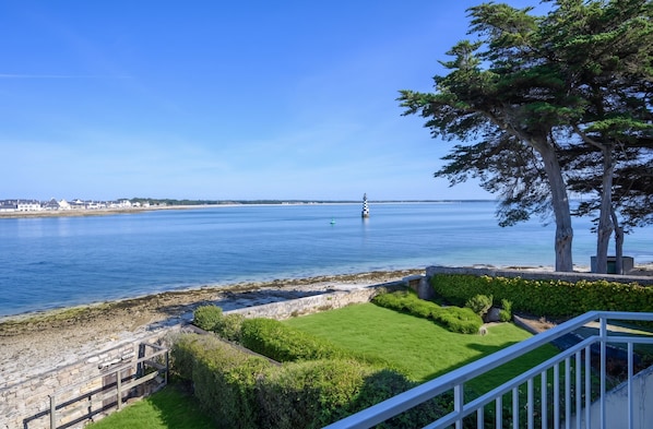 A coastal view with a lighthouse, grassy areas, and a stone wall.