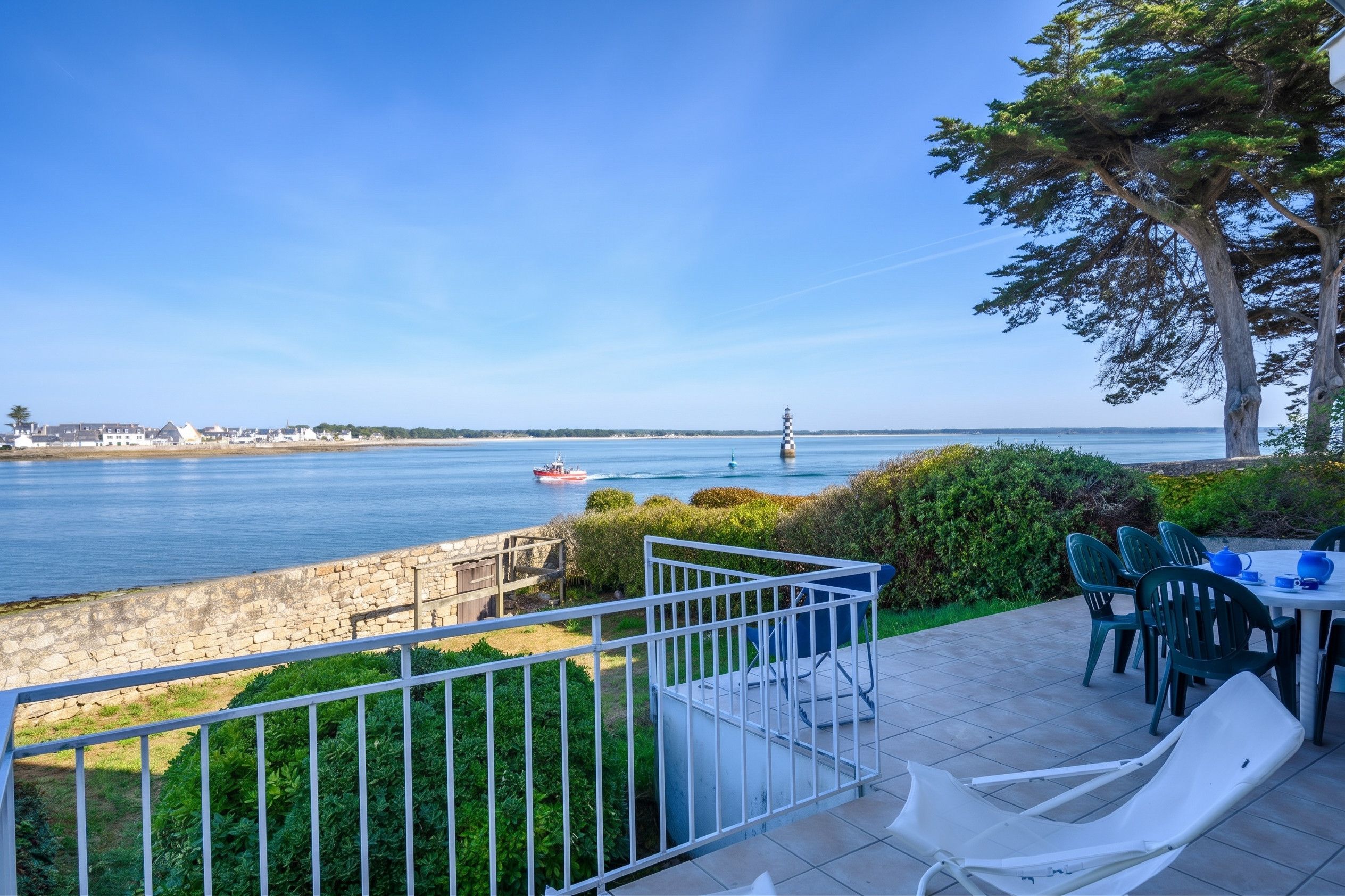 Une terrasse en bord de mer offrant une vue sur la mer, un phare et un mur de pierre.