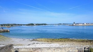 Une vue sur la côte, avec un ciel dégagé, une eau calme et un mur de pierre au premier plan.