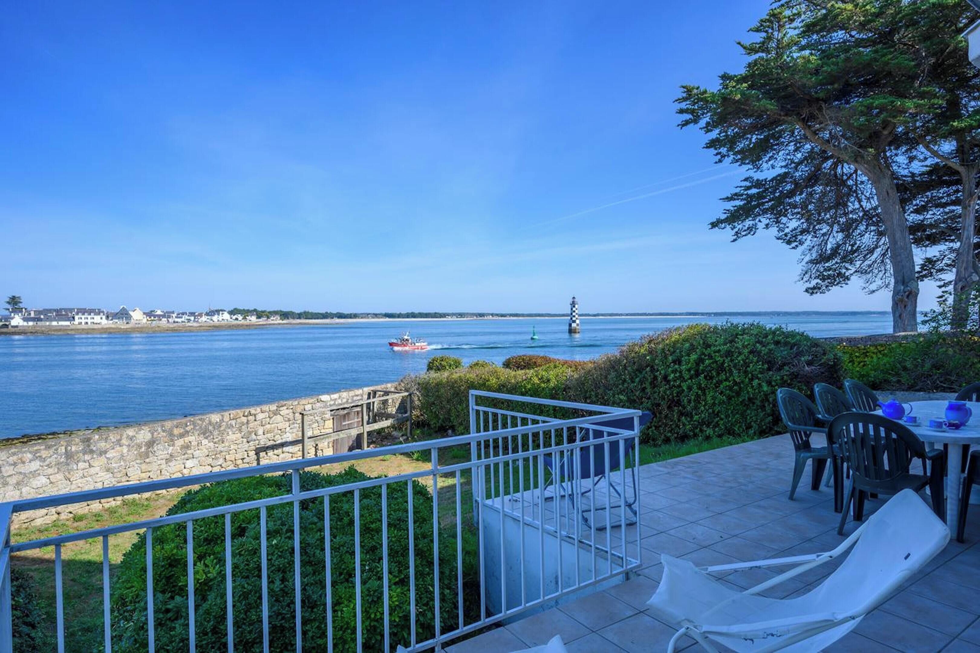 Un balcon avec vue sur la mer, un mur en pierre et une table avec des chaises.