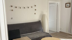 A room with a dark grey sofa, a wooden table, and a round table. There is a string of decorative lights on the wall.