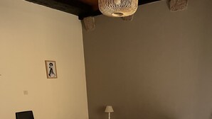 A bedroom with a bed, bench, bedside table, lamp, and a picture on the wall.