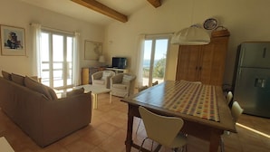 A spacious living room with a sofa, a dining table, and a kitchen area with a refrigerator. - Maison Maquis - the view, the silence, the sea (Sartène)