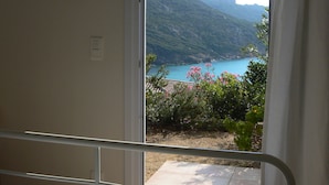 A bedroom with a bed, a window with a view of a mountainous landscape and a body of water. - Maison Maquis - the view, the silence, the sea (Sartène)