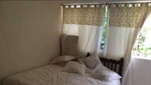 Un dormitorio con cama, almohadas y ventana con cortinas.