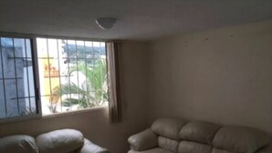 Una habitación con un sofá color beige, una ventana con barrotes y vistas al verde exterior.