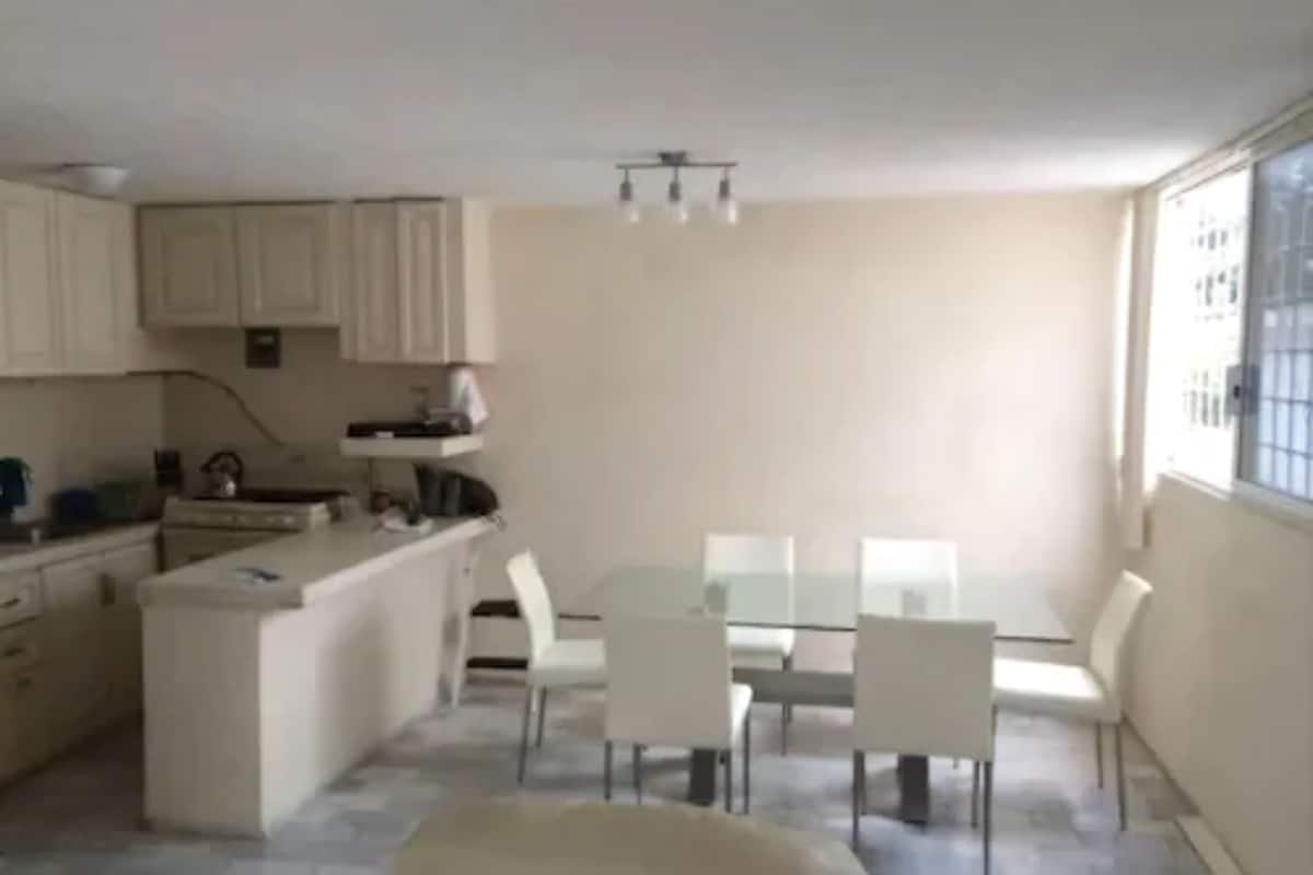 A compact kitchen with white cabinets and a small dining area with a glass table and white chairs.