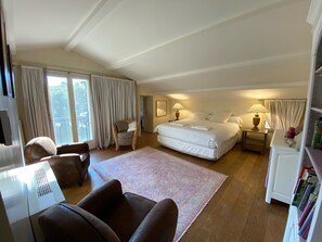 Un dormitorio amplio con una cama grande, una zona de estar con una silla, un escritorio y una estantería.