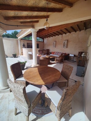 Un patio al aire libre con mobiliario de mimbre, una mesa redonda de madera y suelo de piedra.