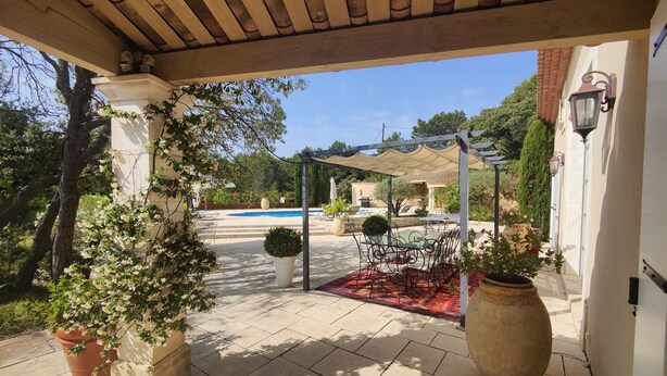 A covered patio area with a pool, outdoor furniture, and potted plants.