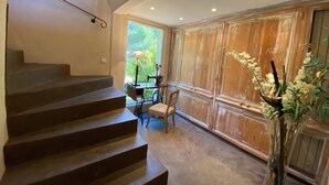 A staircase leading to a room with a table and chairs, a vase with flowers, and a large window with a view of greenery.