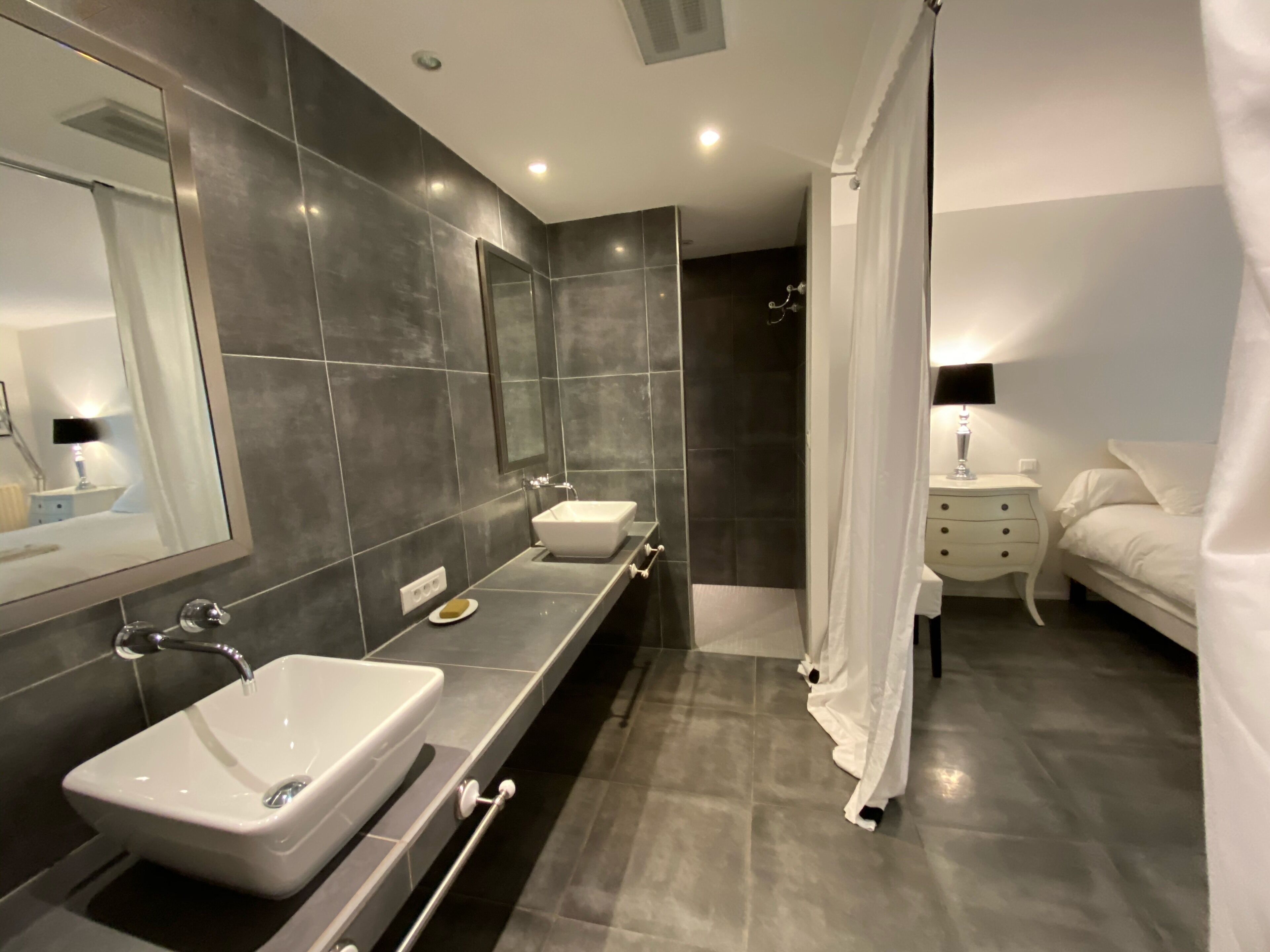 A modern bathroom with two sinks, a large mirror, and a shower area.