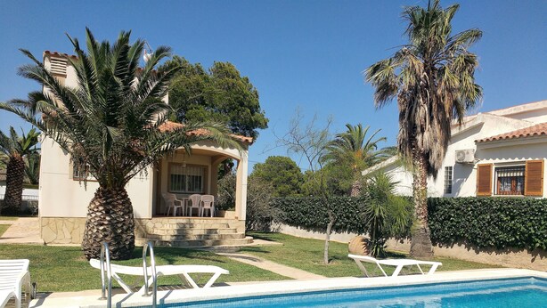 Una piscina con sillas de descanso, un porche techado con sillas y palmeras.