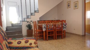 Un comedor con una mesa dispuesta para cuatro personas, una escalera y un sofá.