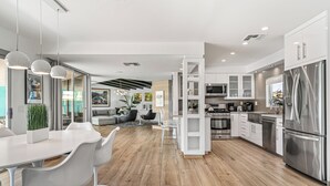 Una cocina moderna con armarios blancos, electrodomésticos de acero inoxidable y un comedor con sillas y mesa en blanco.