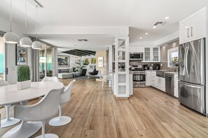 A modern kitchen with white cabinetry, stainless steel appliances, and a dining area with white chairs and a table.
