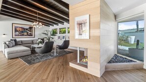 Una sala moderna con un sofá modular, una mesa de centro, una chimenea y un ventanal grande.