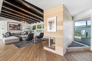 A modern living room with a sectional sofa, a coffee table, a fireplace, and a large window.