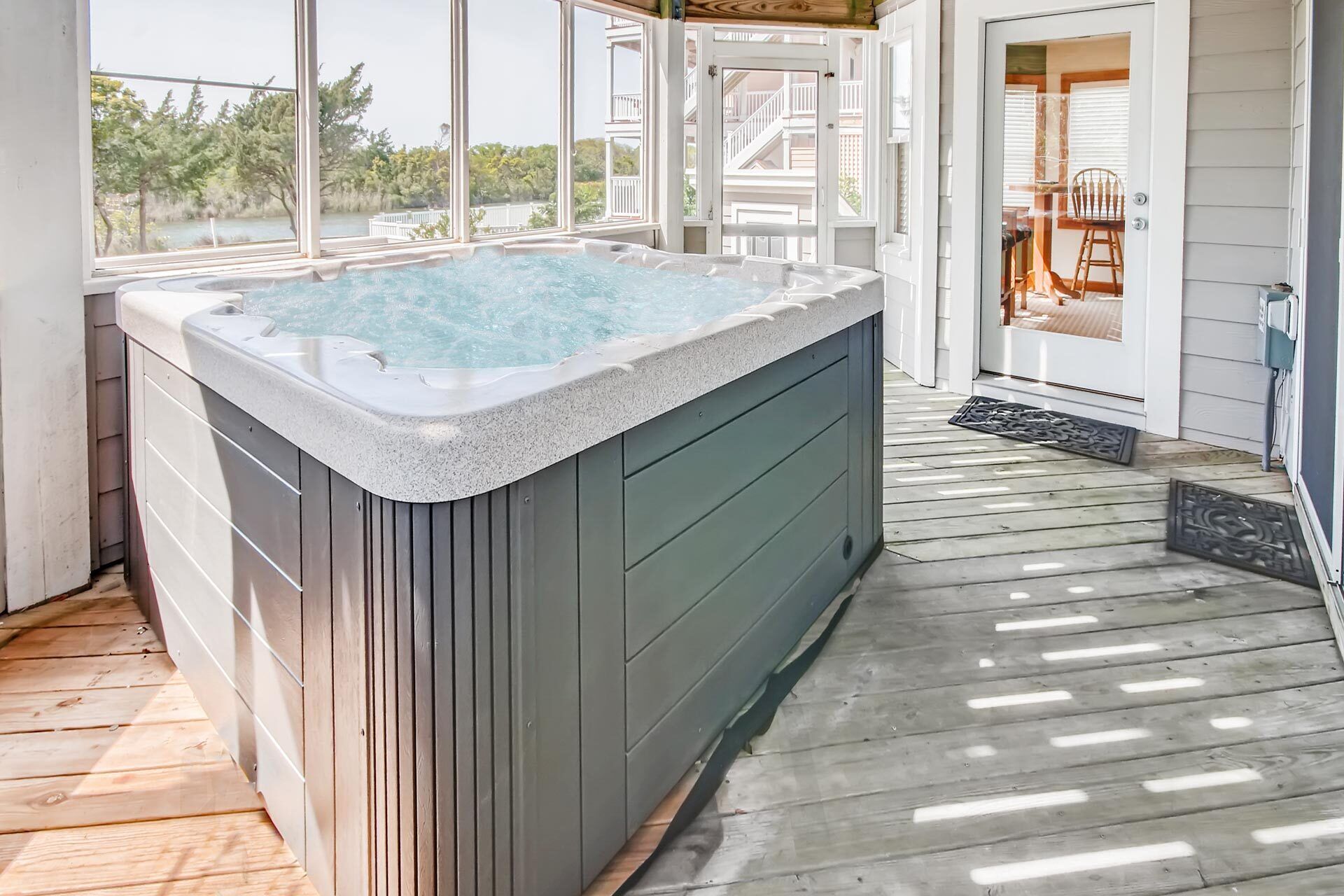 A hot tub on a wooden deck with a view of a lake and buildings.