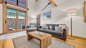 Een ruime woonkamer met een leren bank, een houten salontafel en een groot raam met uitzicht op een besneeuwd landschap.