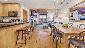 Een ruime keuken met houten kasten, een centraal eiland met krukken, en een eethoek met een houten tafel en stoelen.