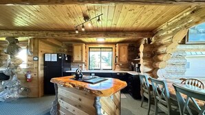 Interior rústico de una cabaña con barra de madera, zona de cocina y asientos.