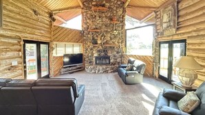 Interior de una cabaña de troncos con chimenea de piedra, sofás de cuero y un televisor de pantalla plana.