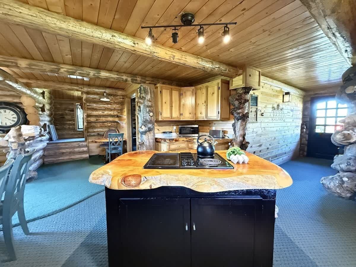 L’intérieur d’un chalet rustique est agrémenté d’un plafond en bois, d’un îlot central avec une bouilloire et d’une cheminée en pierre.