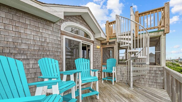 A wooden deck with turquoise Adirondack chairs, a wooden staircase, and a view of the surrounding area. - Oceanview Dog Friendly Home with Private Pool, Hot Tub, Game Room, and Wet Bar (Buxton)