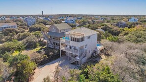 A two-story house with a deck and a swimming pool, surrounded by dense vegetation and other houses. - Oceanview Dog Friendly Home with Private Pool, Hot Tub, Game Room, and Wet Bar (Buxton)