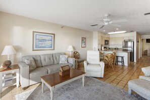 A living room with a sofa, armchairs, a coffee table, and a kitchen in the background.