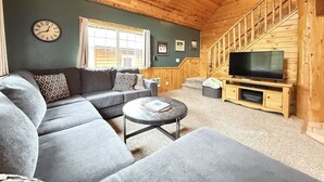 A cozy living room with a sectional sofa, a round coffee table, a flat-screen TV, and a staircase leading to an upper level. - 24 MI to YNP | ATV Trails | Near Big Springs (Island Park)