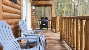 A wooden log cabin with a deck featuring Adirondack chairs and a grill. - 24 MI to YNP | ATV Trails | Near Big Springs (Island Park)