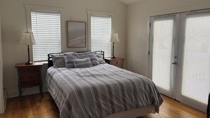 Een slaapkamer met een bed, twee nachtkastjes met lampen, een houten vloer, een plafondventilator en een deur met raam.