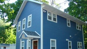 Een blauw huis met twee verdiepingen, een witte veranda en een rode deur.