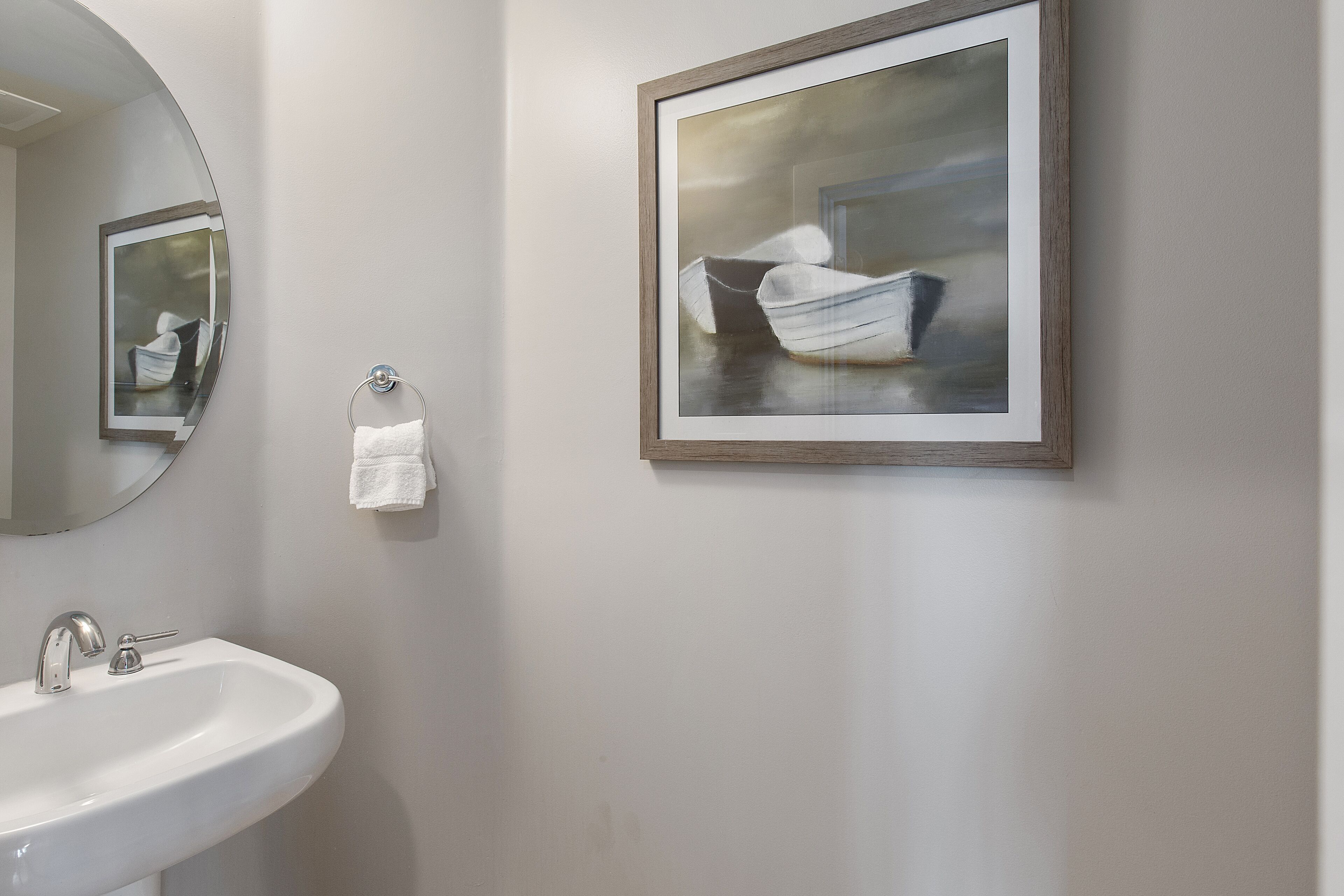 A bathroom with a white sink, a mirror, and a framed painting of a boat.